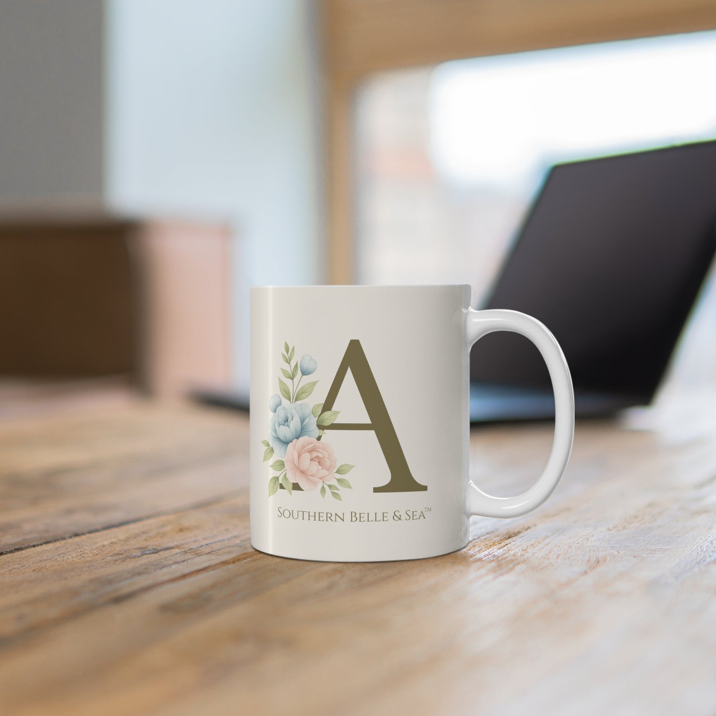 White mug with floral design and letter 'A' on a wooden surface