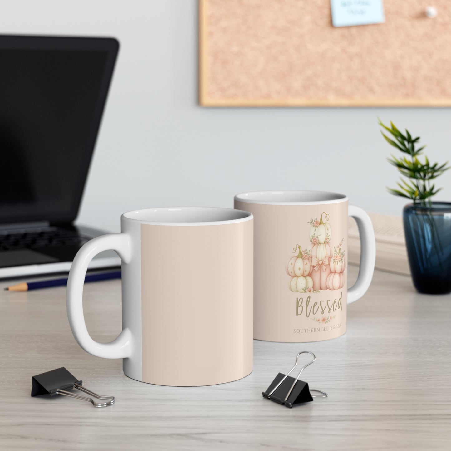 Two mugs on a desk with one featuring a pumpkin design and the word 'Blessed'.