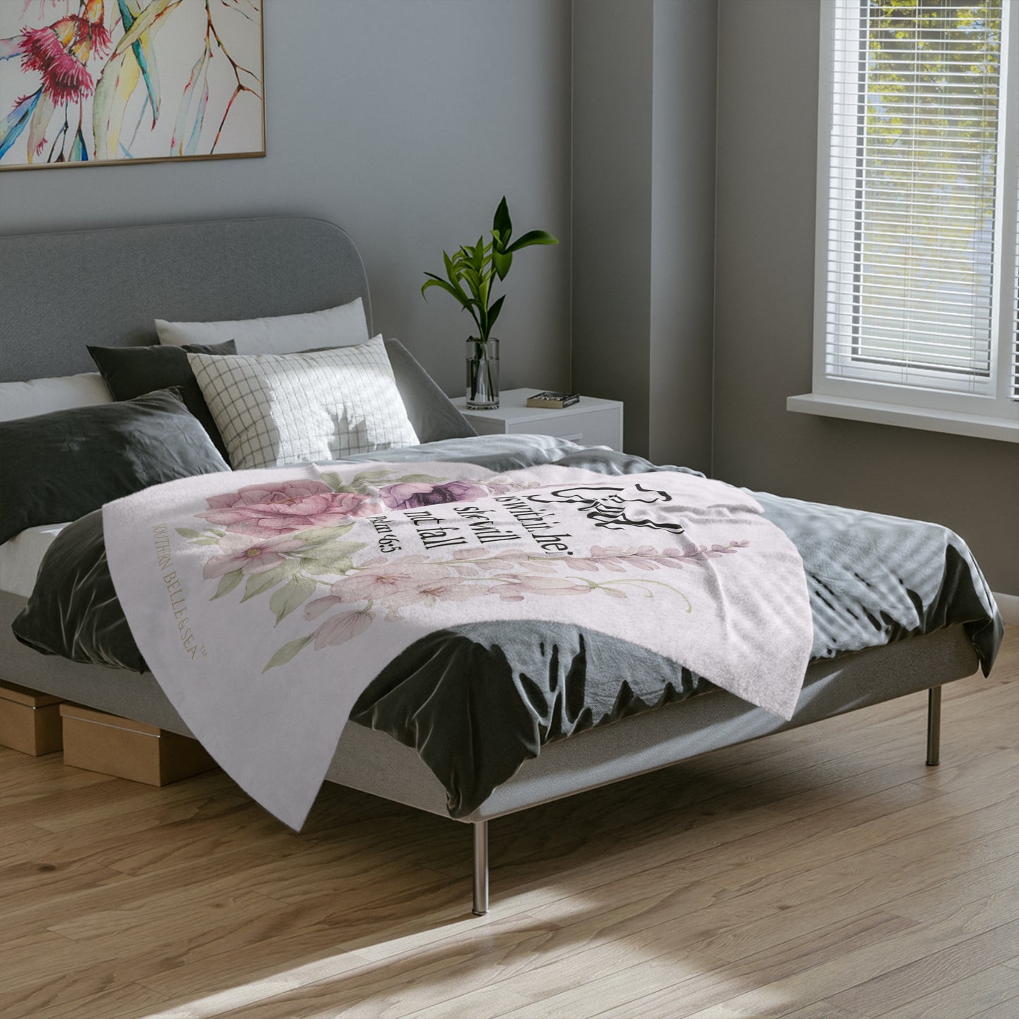 Bedroom with a bed featuring a floral blanket and decorative pillows, with a plant and artwork on the wall.