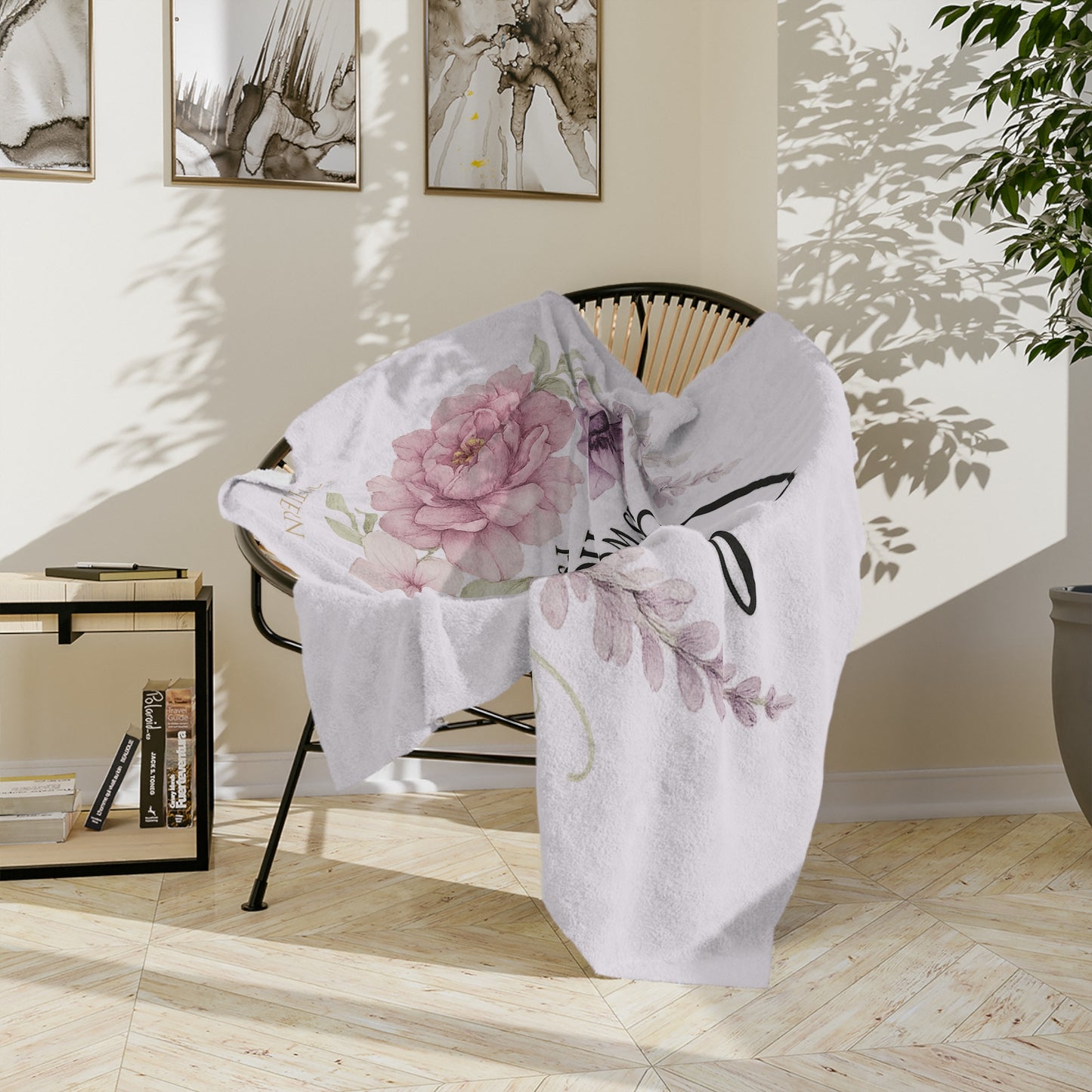 Floral-patterned blanket draped over a chair in a room with light wood flooring and framed artwork on the wall.