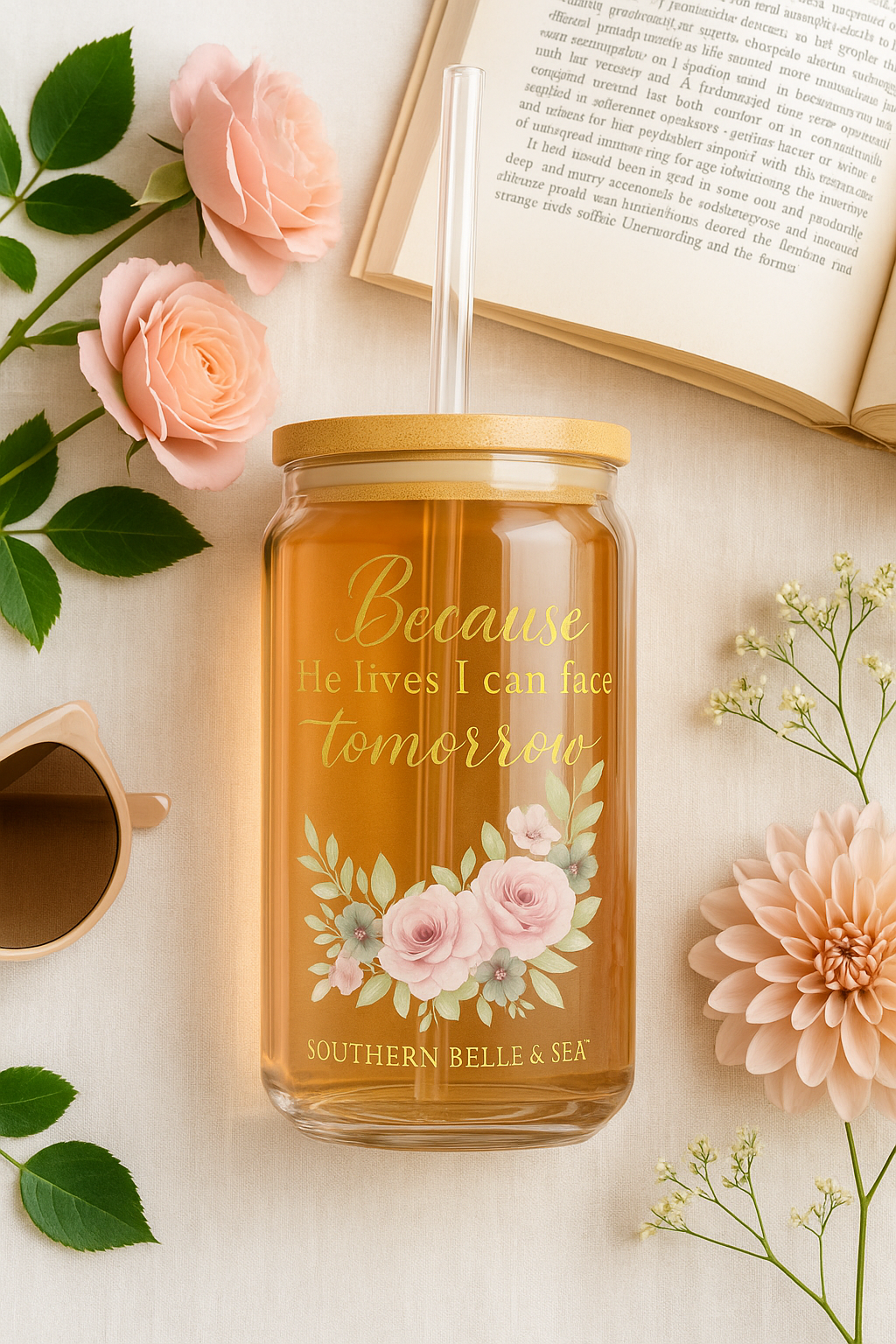 Jar of tea with floral design and text, surrounded by flowers and a book on a light surface.