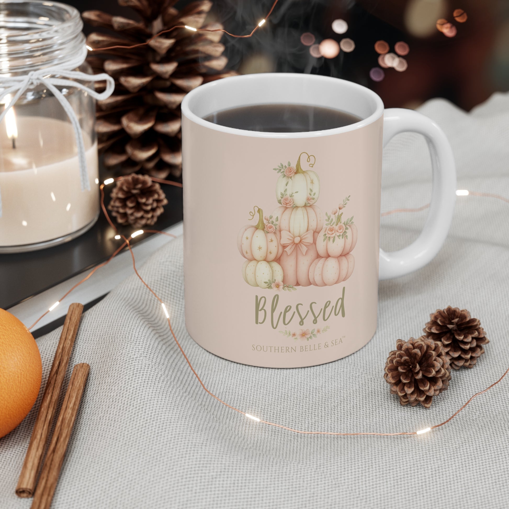 Mug with pumpkin design and 'Blessed' text on a table with candles and pinecones.