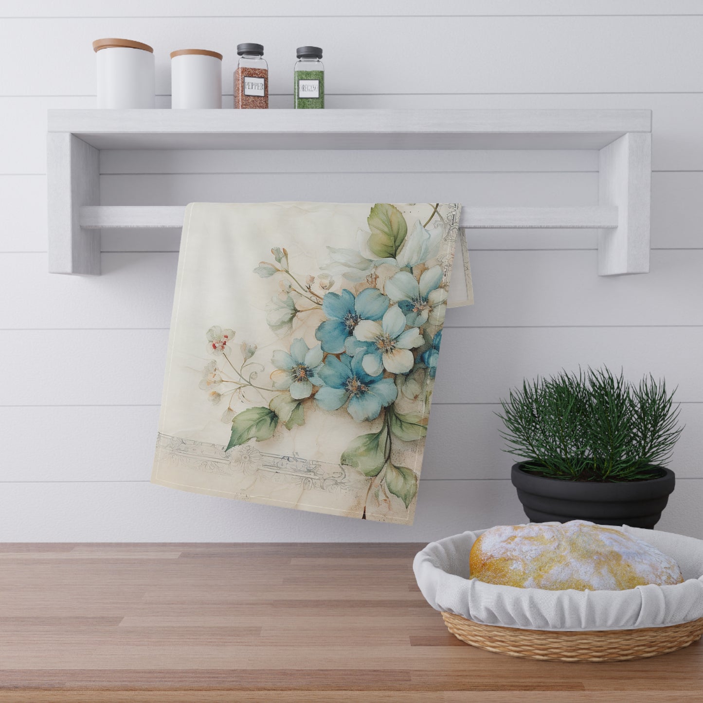 Floral dogwood blue towel hanging on a rack with a basket of bread and a plant in the background.