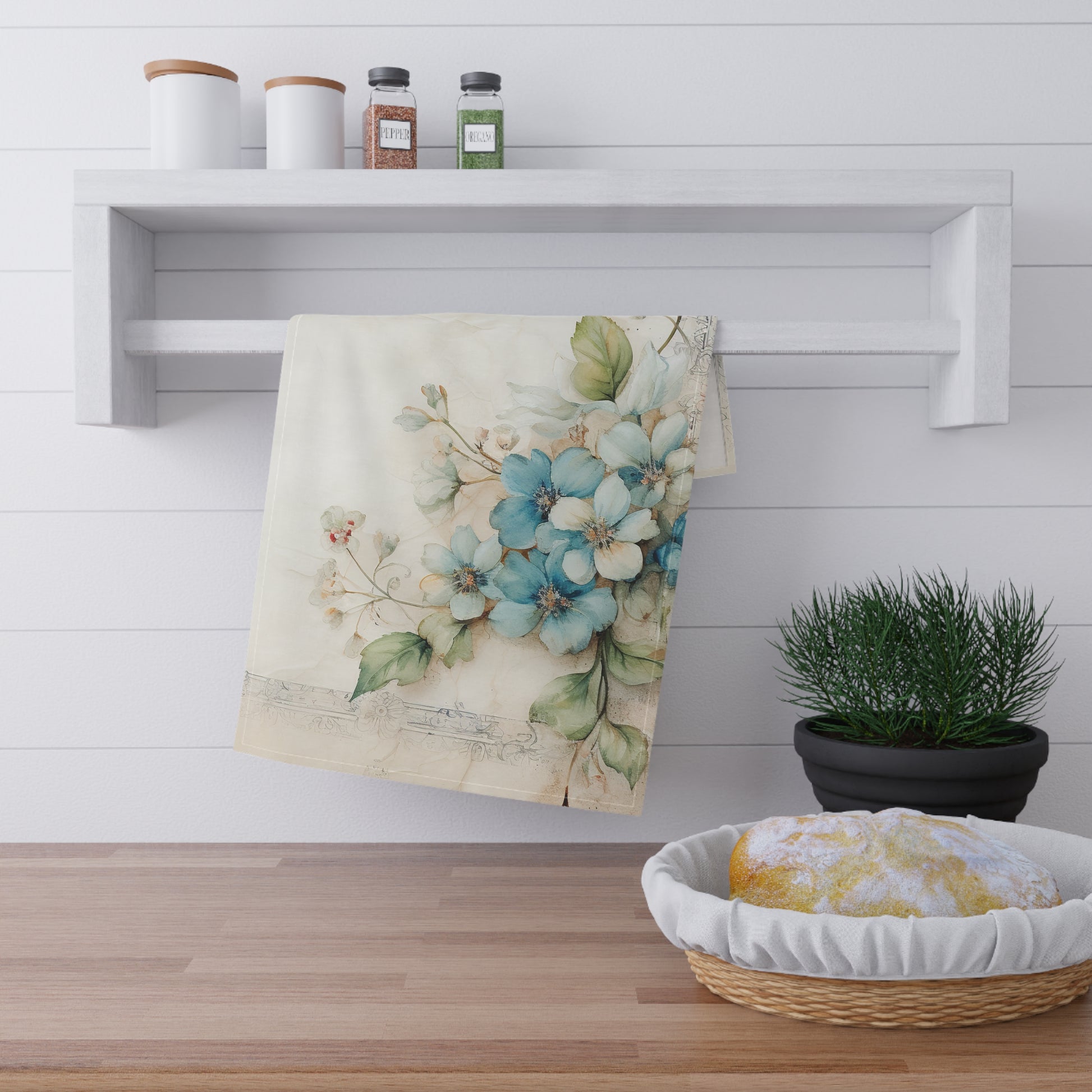 Floral dogwood blue towel hanging on a rack with a basket of bread and a plant in the background.