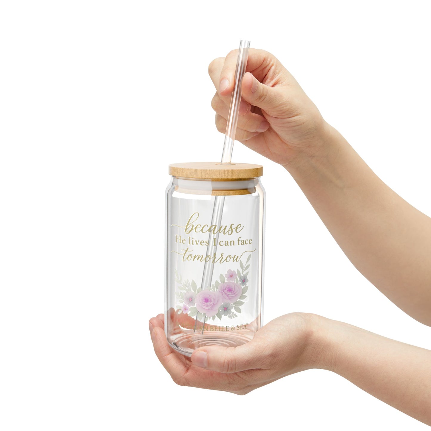 Glass tumbler with straw and floral design held by a hand on a white background