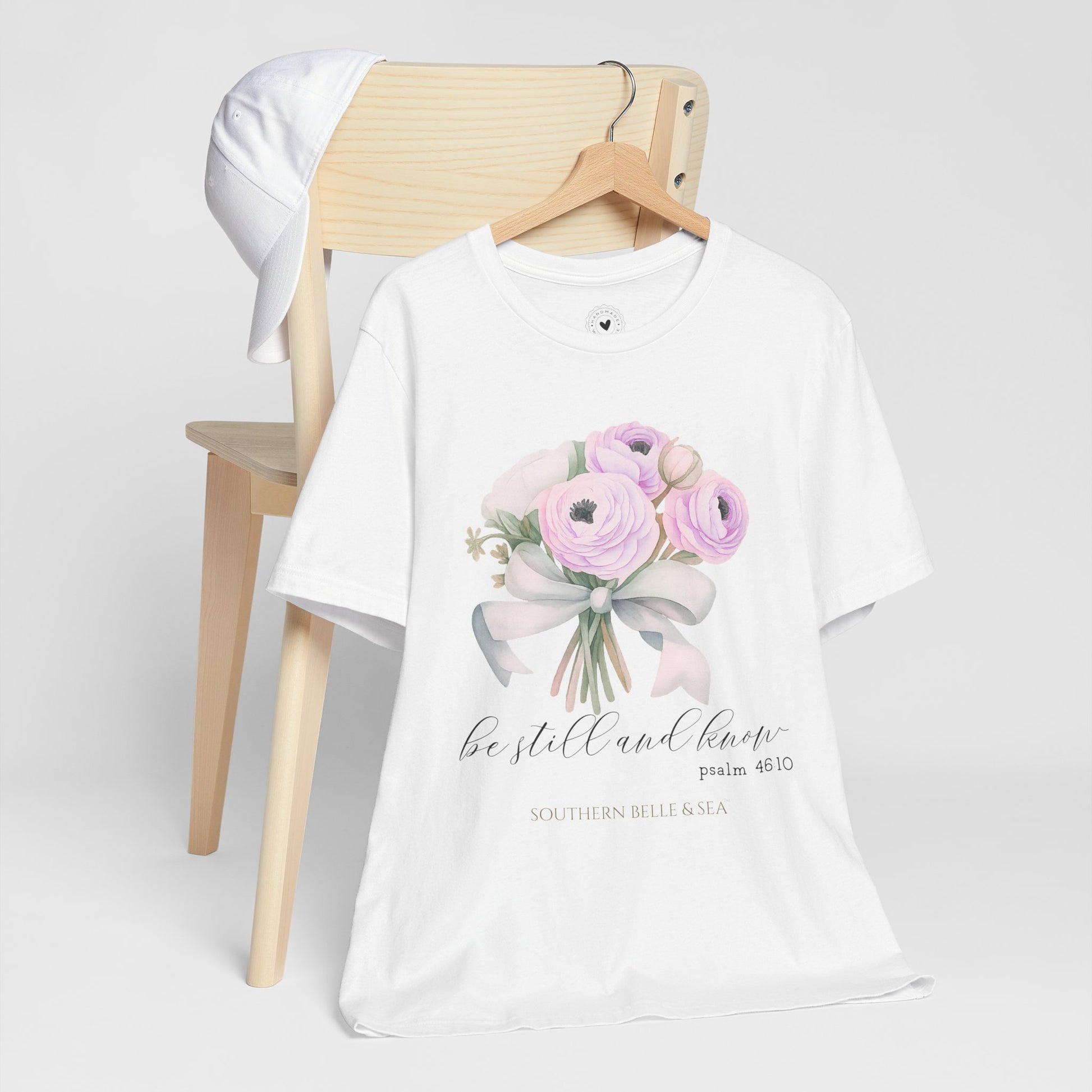 White t-shirt with floral design and text on a wooden chair against a white background