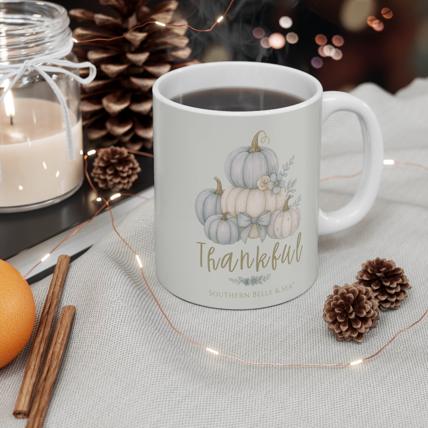 White mug with pumpkin design and 'Thankful' text, surrounded by autumn decorations on a table.