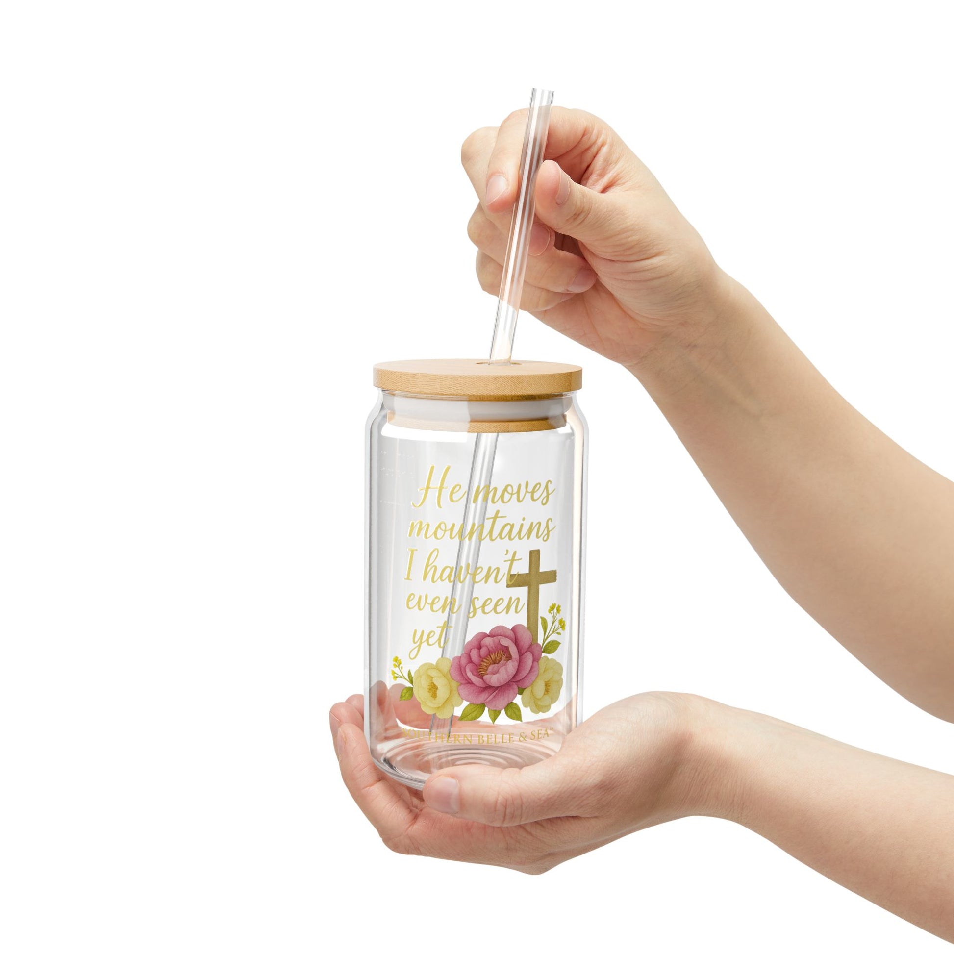 Glass tumbler with wooden lid and floral design held by a hand on a white background