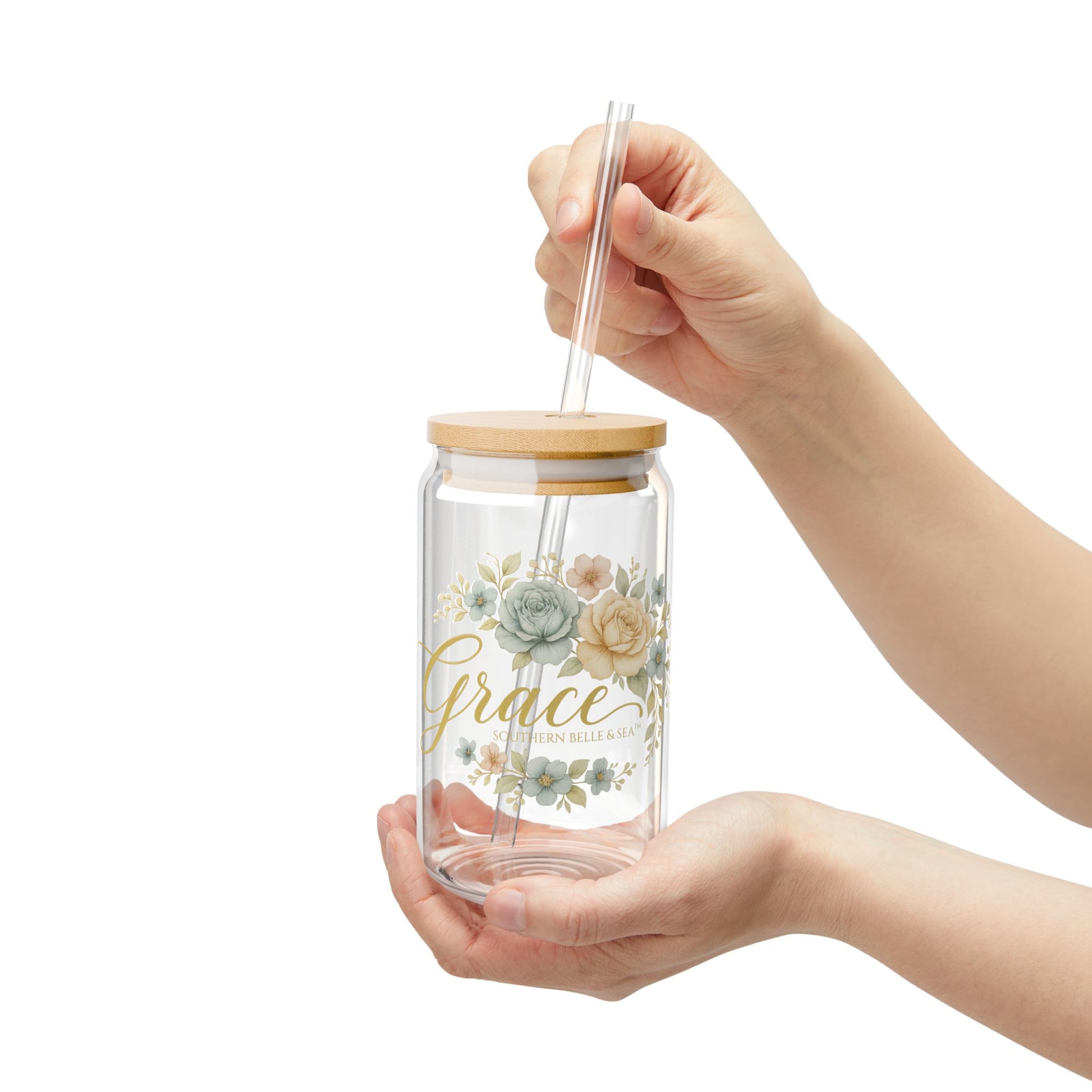 Glass tumbler with floral design and 'grace' text, held by a hand on a white background