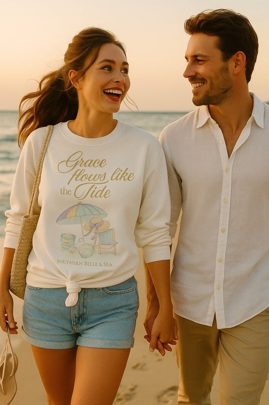 Woman smiling at the beach in white sweatshirt reading “Grace Flows Like the Tide” by Southern Belle & Sea™