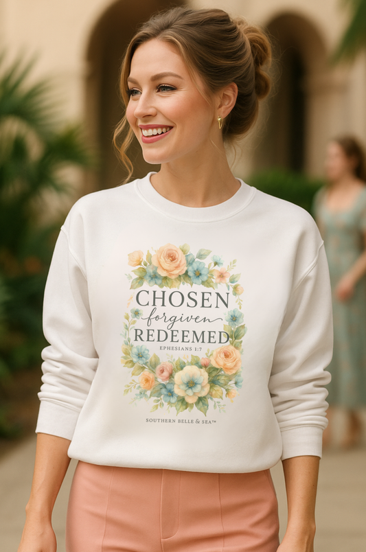 Woman smiling in white Christian sweatshirt with soft floral design and Bible verse “Chosen, Forgiven, Redeemed – Ephesians 1:7” by Southern Belle & Sea™.
