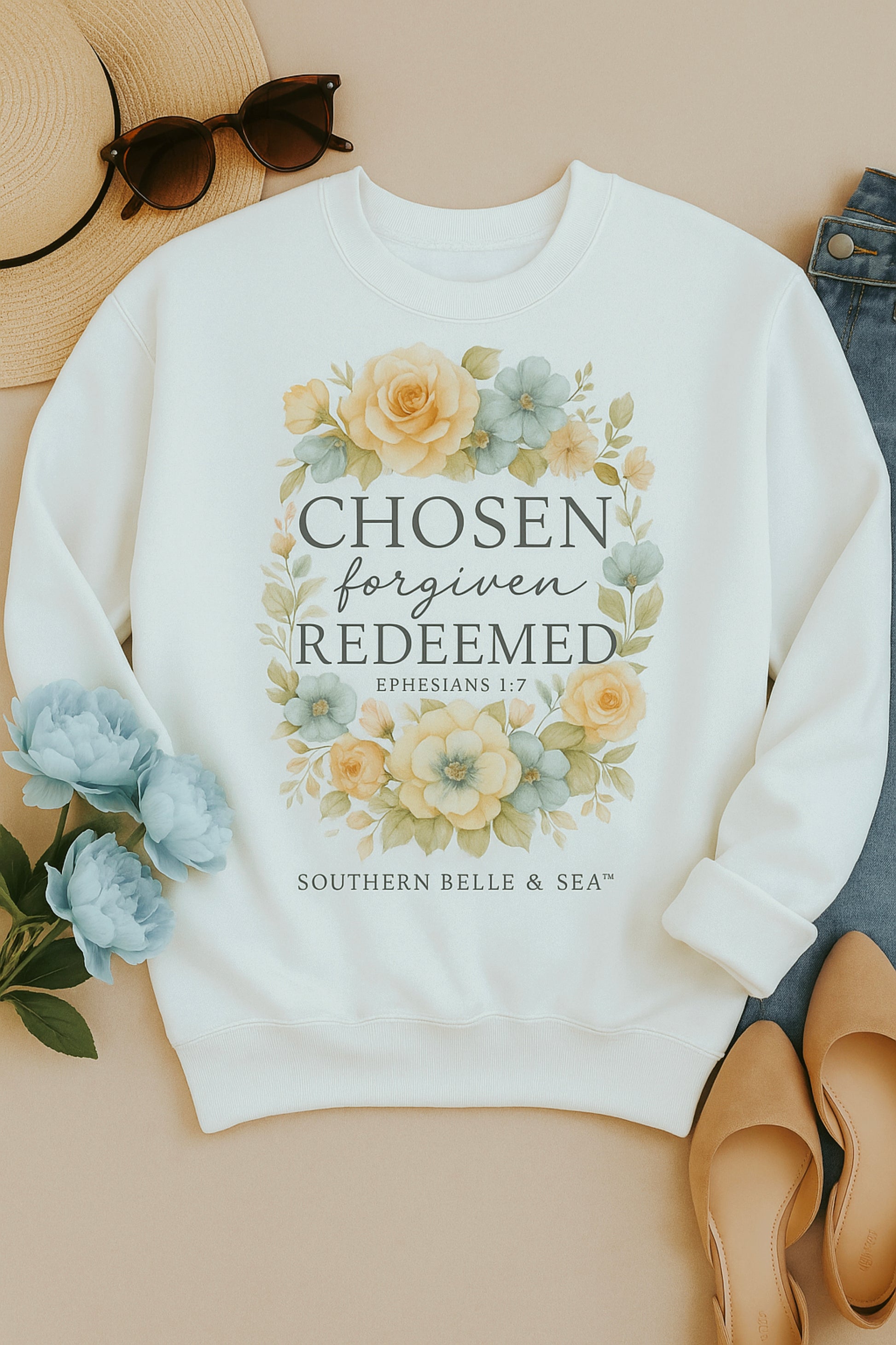 White sweatshirt with floral design and text on a beige surface with accessories.